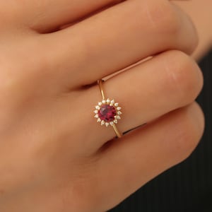 May include: A gold ring featuring a red gemstone encircled by a halo of smaller white gemstones.