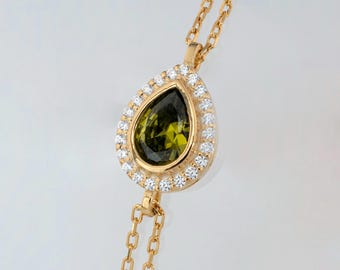 May include: A gold chain necklace with a pear-shaped green gemstone pendant surrounded by a halo of small clear stones.