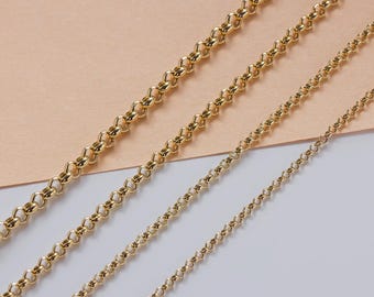 May include: Three gold chains of different lengths, laid out on a beige and white surface. The chains are made of small, round links.