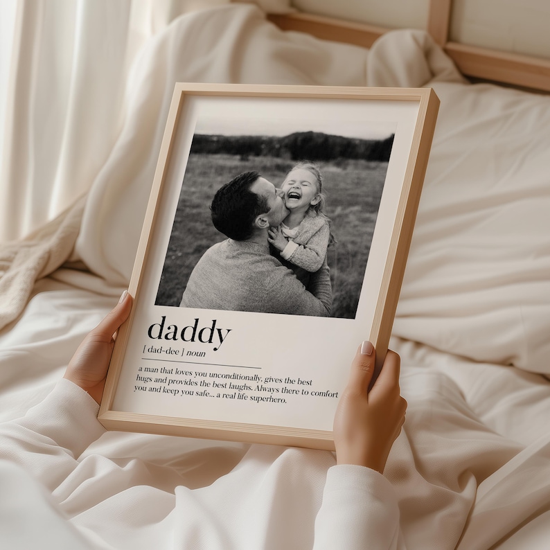 K&ouml;nnte beinhalten: Gerahmtes Schwarz-Wei&szlig;-Foto mit einem Mann und einem Kind, das lacht. Das Wort "daddy" ist darunter zusammen mit einer Definition abgedruckt. Der Rahmen ist aus hellem Holz.