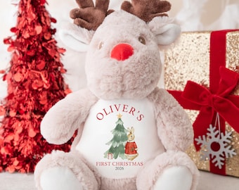 May include: A plush reindeer toy with soft light brown fur, dark brown antlers, and a bright red nose. The white belly panel features a printed graphic of a Christmas tree and a rabbit, with the text OLIVER'S FIRST CHRISTMAS 2026.
