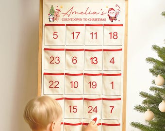 Puede incluir: Un calendario de adviento navideño color crema con ribetes rojos y bolsillos numerados del 1 al 24. El calendario está personalizado con el nombre "Amelia's" e ilustraciones festivas. Un niño interactúa con el calendario.