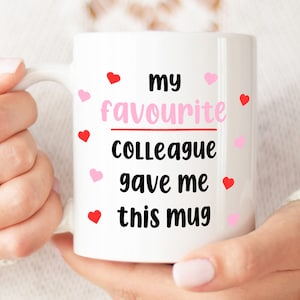 Pode incluir: Caneca de cer&acirc;mica branca com texto preto que diz "my favourite colleague gave me this mug". O texto &eacute; cercado por cora&ccedil;&otilde;es rosa e vermelhos.