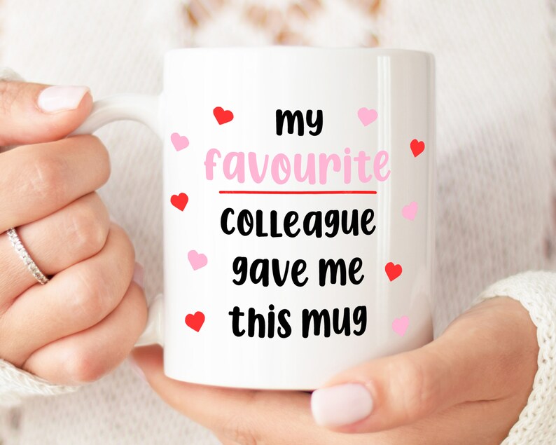 Pode incluir: Caneca de cer&acirc;mica branca com texto preto que diz "my favourite colleague gave me this mug". O texto &eacute; cercado por cora&ccedil;&otilde;es rosa e vermelhos.