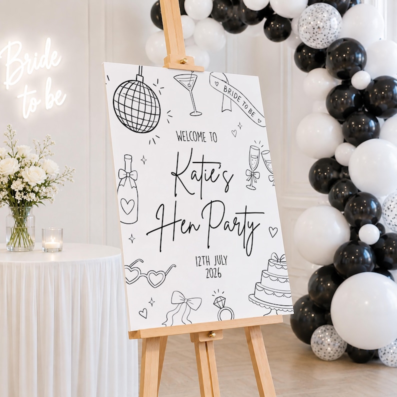 May include: A white sign on a wooden easel with black line art illustrations and text. The sign reads "Welcome to Katie's Hen Party 12th July 2026." A neon sign that says "Bride to be" is in the background. Black and white balloons decorate the background.