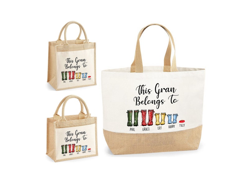 May include: Two tote bags with a jute bottom and a white canvas top. The bags have a black print that says "This Gran Belongs To" with a row of colorful rain boots and names underneath. The smaller bag has the names Phil, Grace, Lily, Harry, and Tilly. The larger bag has the names Phil, Grace, Lily, Harry, and Tilly.