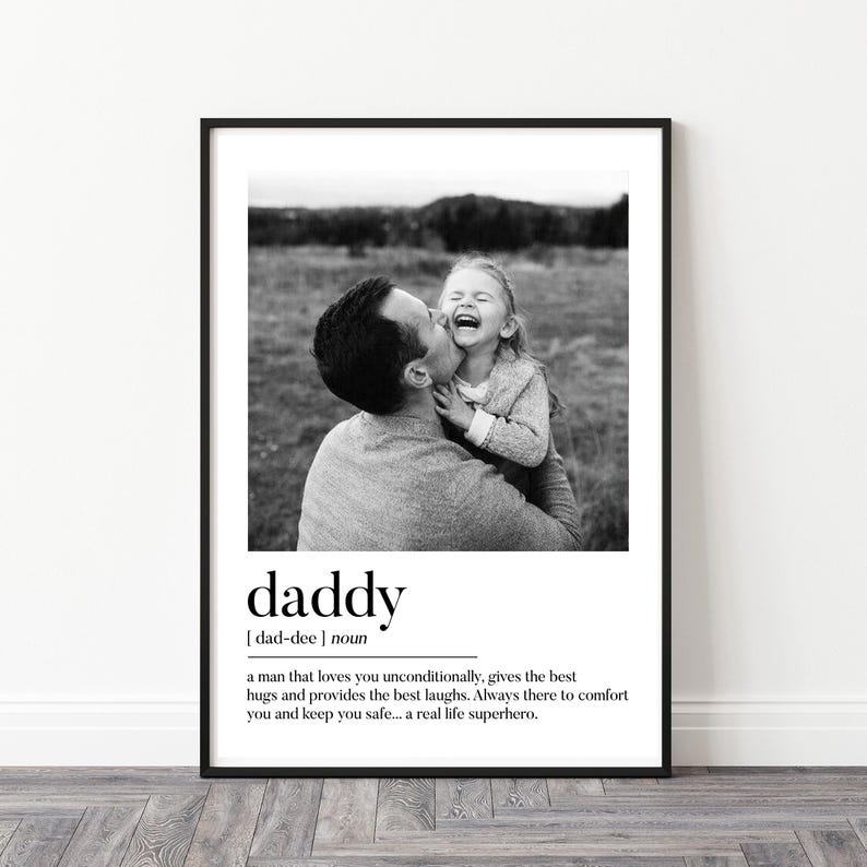 K&ouml;nnte beinhalten: Schwarz-Wei&szlig;-Druck mit Rahmen, der einen Vater zeigt, der sein Kind k&uuml;sst, beide lachen. Das Wort "daddy" ist unter dem Foto zusammen mit einer Definition abgedruckt. Ein herzerw&auml;rmendes Wandkunstwerk.