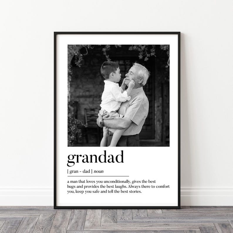 May include: Black and white framed print featuring a grandfather holding a child. The word "grandad" is printed below the image, along with a definition. The image shows a loving moment between the two.