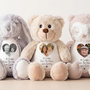 Puede incluir: Tres animales de peluche: un conejito gris, un oso de peluche beige y un oso rosa. Cada uno tiene una foto en forma de corazón y el texto "A Cuddle From The Stars" con un nombre debajo. El oso de peluche tiene una nariz marrón.