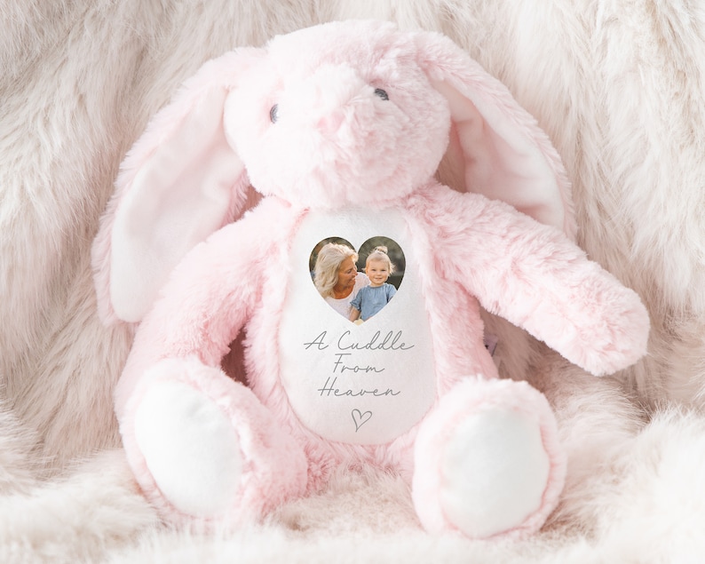 Puede incluir: Conejo de peluche rosa con un parche blanco en forma de coraz&oacute;n. El parche tiene una foto de una mujer y un ni&ntilde;o y el texto "A Cuddle From Heaven".