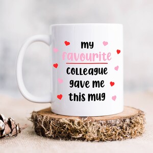 Pode incluir: Caneca de cer&acirc;mica branca com o texto "my favourite colleague gave me this mug" em letras pretas e cora&ccedil;&otilde;es rosa ao redor do texto.