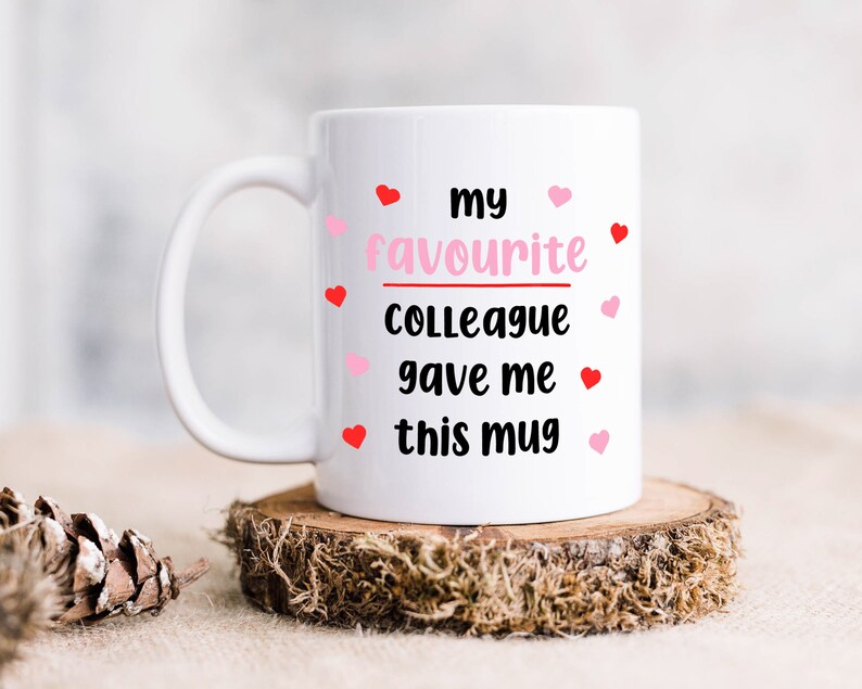 Pode incluir: Caneca de cer&acirc;mica branca com o texto "my favourite colleague gave me this mug" em letras pretas e cora&ccedil;&otilde;es rosa ao redor do texto.
