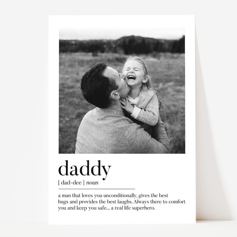 K&ouml;nnte beinhalten: Schwarz-Wei&szlig;-Druck mit einem Vater, der sein lachendes Kind k&uuml;sst. Das Wort "daddy" ist unter dem Bild abgebildet, zusammen mit einer Definition, die einen liebevollen Vater beschreibt. Der Hintergrund zeigt eine verschwommene Szene im Freien.