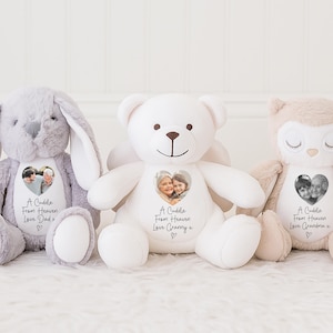 May include: Three soft toys: a grey bunny, a white teddy bear, and a beige owl. Each has a photo in a heart shape and the text "A Cuddle From Heaven" with a name below. The bunny says "Love Dad", the bear says "Love Granny", and the owl says "Love Grandma".