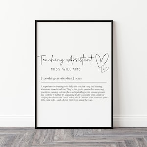 May include: A framed print featuring the words "Teaching Assistant" in elegant script, with a heart symbol. Below, it reads "MISS WILLIAMS" and a definition of a teaching assistant. The print is in a black frame.