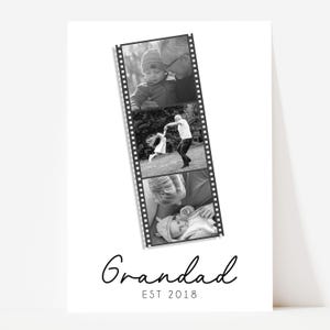 May include: Black and white print featuring a film strip of family photos. The word "Grandad" is written in cursive, with "EST 2018" below. The film strip shows a baby with a grandparent, a child dancing, and a baby being held.