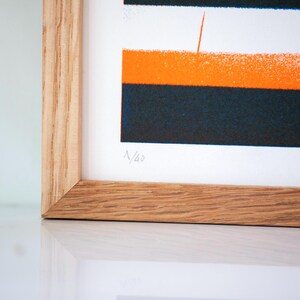 May include: A framed print with a geometric design in orange, black, and white. The print is numbered "N/43".