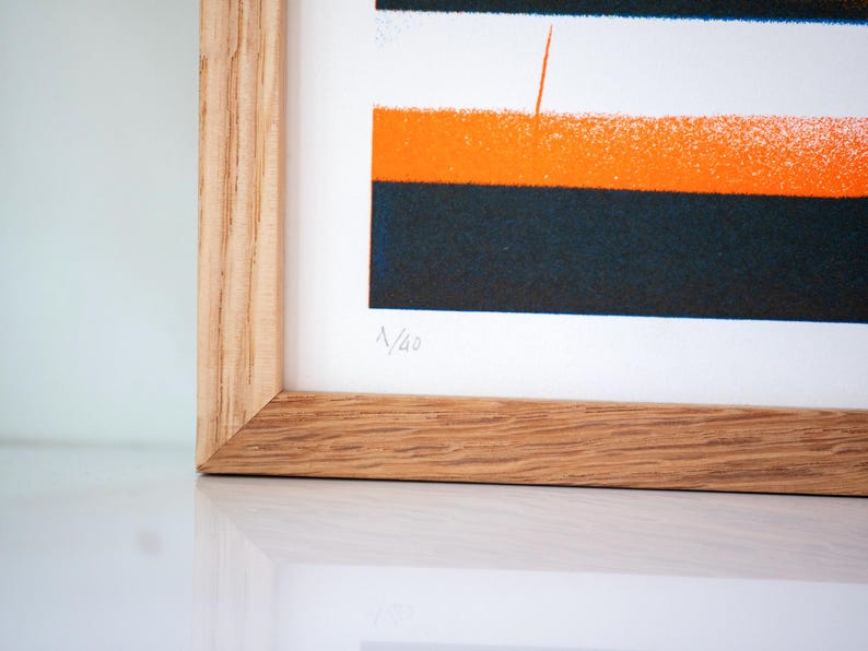 May include: A framed print with a geometric design in orange, black, and white. The print is numbered "N/43".