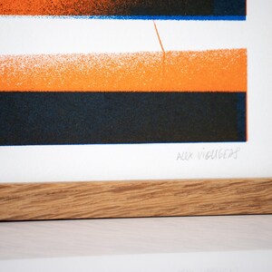May include: A framed print with a geometric design in orange, blue, and black. The print is signed "Alex Vigus 20".