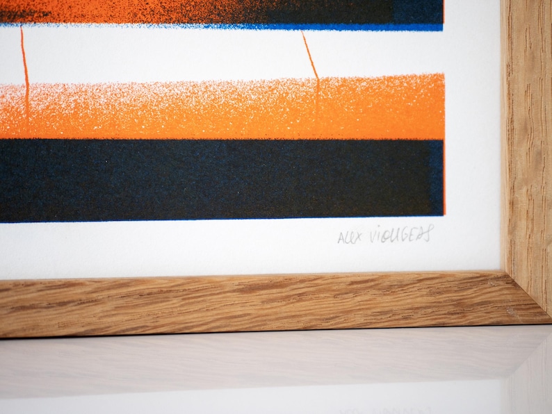 May include: A framed print with a geometric design in orange, blue, and black. The print is signed "Alex Vigus 20".