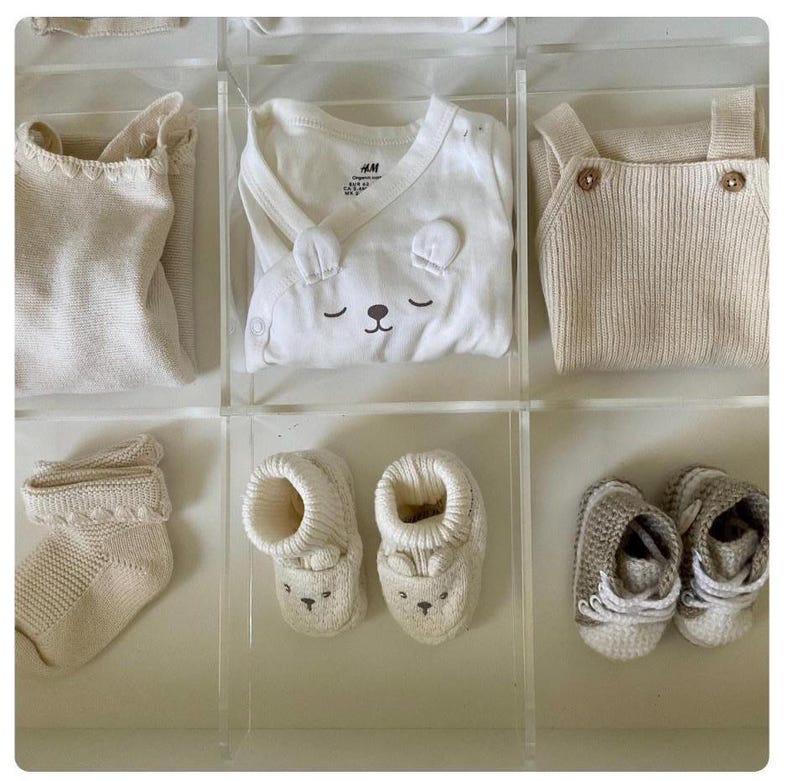 Puede incluir: Un conjunto de ropa y accesorios para beb&eacute; en tonos blancos y crema. El conjunto incluye un body blanco con un dise&ntilde;o de oso, un jersey de punto crema, un par de calcetines de punto crema y un par de botines de punto crema.