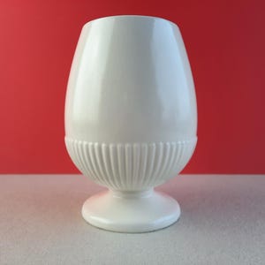 May include: A white ceramic vase with a fluted design and a round base. The vase is empty and has a glossy finish.
