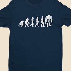 May include: A navy blue t-shirt with a white graphic showing the evolution of humans, ending with a robot. The design shows a progression from ape to robot. A crew neck, short-sleeved shirt.