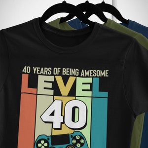 Op de afbeelding: Zwart T-shirt met een retro-grafisch ontwerp met een videogamecontroller en de tekst "40 YEARS OF BEING AWESOME LEVEL 40 UNLOCKED".