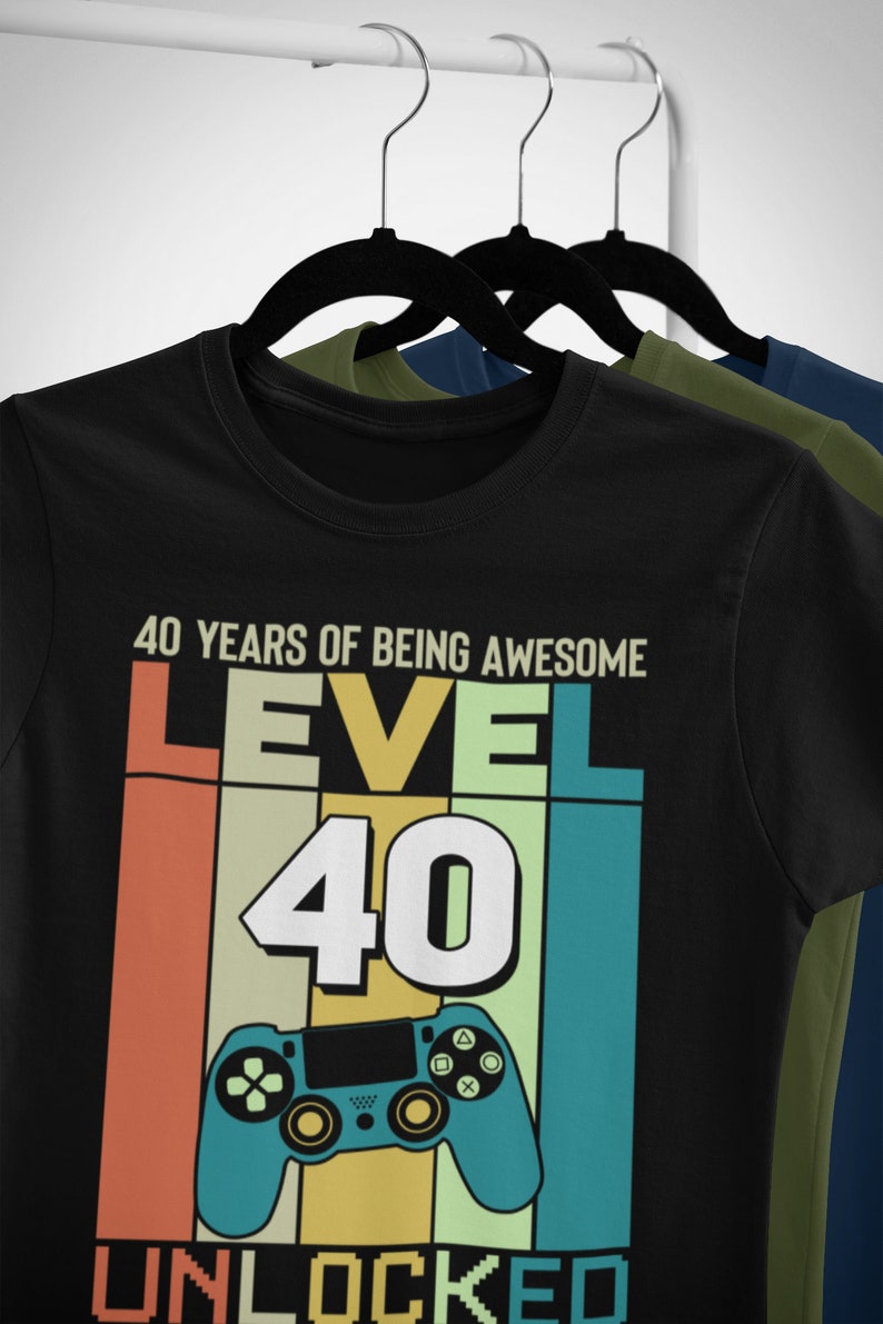 Op de afbeelding: Zwart T-shirt met een retro-grafisch ontwerp met een videogamecontroller en de tekst "40 YEARS OF BEING AWESOME LEVEL 40 UNLOCKED".