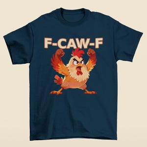 May include: Navy blue t-shirt featuring a cartoon chicken with raised wings and an angry expression. The text "F-CAW-F" is printed above the chicken in a retro font. The chicken is primarily orange, red, and yellow.
