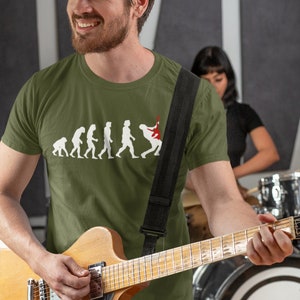 May include: A man wearing a green t-shirt with a graphic of the evolution of man culminating in a person playing an electric guitar. He is holding a brown electric guitar and smiling.