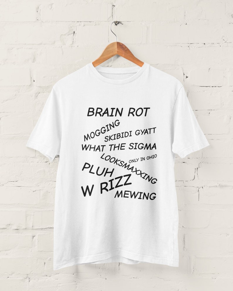 May include: White t-shirt with black text that reads "BRAIN ROT", "MOGGING", "SKIBIDI GYATT", "WHAT THE SIGMA", "ONLY IN OHIO", "LOOKSMAXXING", "PLUH", "W RIZZ", and "MEWING".