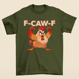 May include: Olive green t-shirt featuring a cartoon chicken with raised fists and an angry expression. The text "F-CAW-F" is printed above the chicken in a retro font. The chicken has red, orange, and yellow feathers.