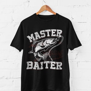 May include: A black short-sleeve t-shirt featuring a white graphic of a fish on a fishing line. The text "MASTER" is printed above the fish and "BAITER" is printed below the fish in a distressed, block-style font. The design includes a red accent.