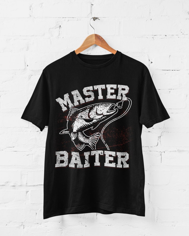 May include: A black short-sleeve t-shirt featuring a white graphic of a fish on a fishing line. The text "MASTER" is printed above the fish and "BAITER" is printed below the fish in a distressed, block-style font. The design includes a red accent.