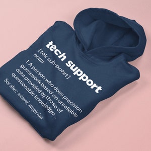 Op de afbeelding: Marineblauwe hoodie met de witte tekst "tech support" en een definitie. De definitie beschrijft een persoon die giswerk doet op basis van onbetrouwbare gegevens. De hoodie vermeldt ook "wizard, magician" als gerelateerde termen.