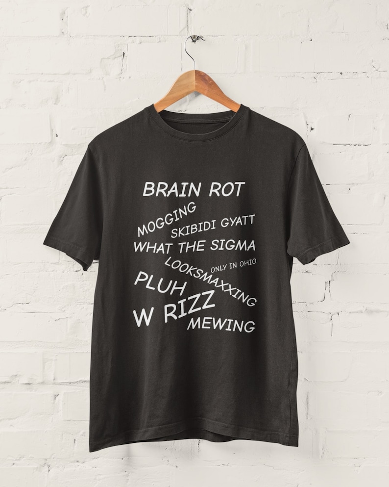 May include: Black t-shirt with white text that reads "BRAIN ROT", "MOGGING", "SKIBIDI GYATT", "WHAT THE SIGMA", "ONLY IN OHIO", "LOOKSMAXXING", "PLUH", "W RIZZ", and "MEWING".