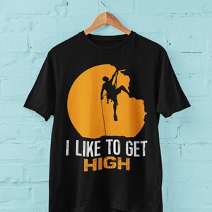 May include: Black t-shirt with a silhouette of a rock climber ascending a cliff face, set against a yellow sun. The text "I like to get HIGH" is printed below the image.
