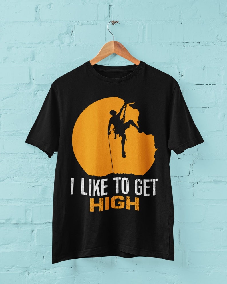 May include: Black t-shirt with a silhouette of a rock climber ascending a cliff face, set against a yellow sun. The text "I like to get HIGH" is printed below the image.