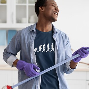 May include: A man wearing a blue shirt with a white graphic of the evolution of humans holding a blue and white mop. He is wearing purple gloves and smiling.