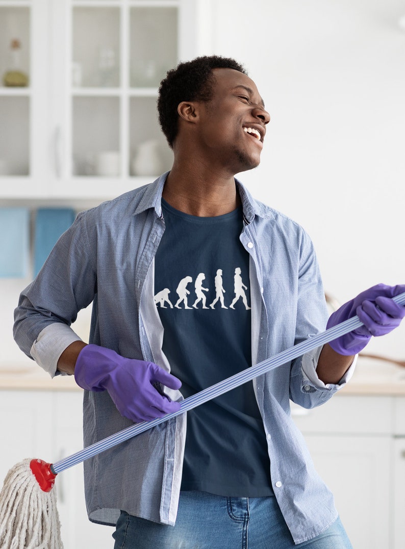 May include: A man wearing a blue shirt with a white graphic of the evolution of humans holding a blue and white mop. He is wearing purple gloves and smiling.