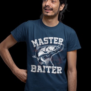 May include: A navy blue short-sleeved t-shirt featuring a white graphic of a fish on a fishing line. The text "MASTER BAITER" is printed in a distressed white font above and below the fish illustration, with subtle red accents.