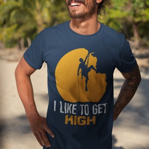 May include: A navy blue t-shirt with a yellow sun graphic and a silhouette of a person rock climbing. The text "I like to get high" is printed in white below the graphic.