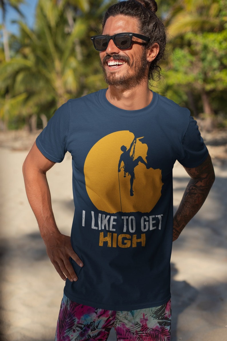 May include: A navy blue t-shirt with a yellow sun graphic and a silhouette of a person rock climbing. The text "I like to get high" is printed in white below the graphic.