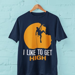 May include: A navy blue t-shirt with a silhouette of a rock climber ascending a cliff face. The climber is silhouetted against a yellow circle. The text "I like to get HIGH" is printed below the image.