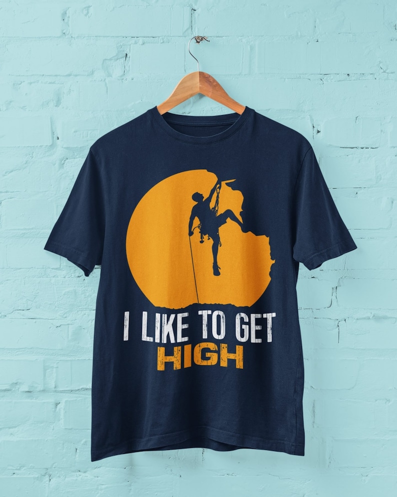 May include: A navy blue t-shirt with a silhouette of a rock climber ascending a cliff face. The climber is silhouetted against a yellow circle. The text "I like to get HIGH" is printed below the image.
