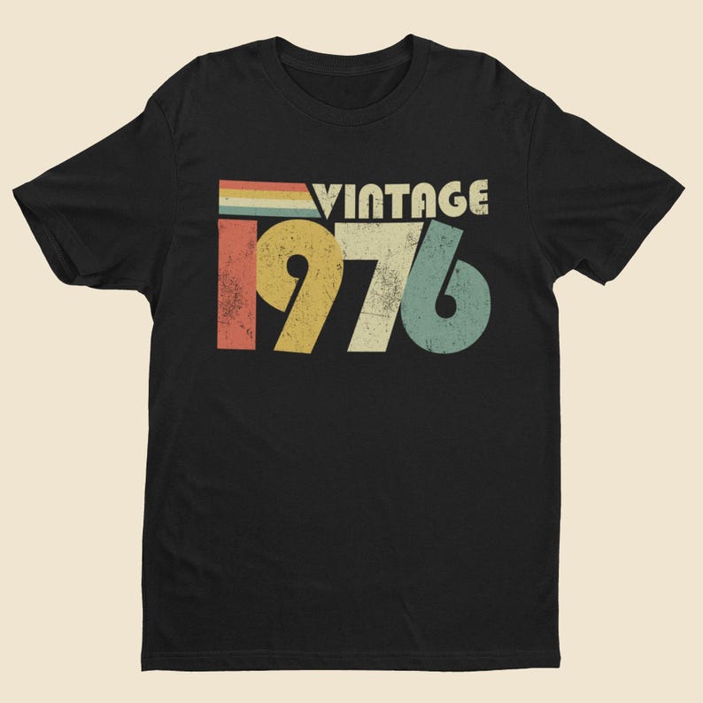 May include: A black short-sleeved t-shirt featuring a distressed graphic print on the chest. The design includes the text VINTAGE in white letters above the large numbers 1976, which are colored in red, yellow, beige, and teal with a worn texture.