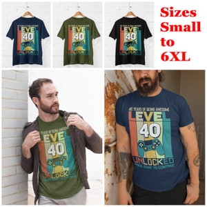 Op de afbeelding: Een blauw, groen en zwart T-shirt met een retro videogame-ontwerp. Het shirt zegt "40 Years of Being Awesome Level 40 Unlocked Press Start to Continue".