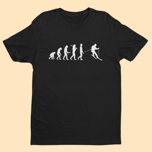 Könnte beinhalten: Schwarzes T-Shirt mit einem weißen Aufdruck, der die Evolution des Menschen darstellt und mit einem Skifahrer endet. Das Design zeigt die Stadien der menschlichen Evolution, die zu einer Skifahrer-Silhouette führen. Eine humorvolle Interpretation der Ski-Evolution.