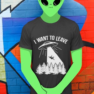 May include: A green alien wearing a black t-shirt with a white graphic of a UFO and the text "I WANT TO LEAVE".